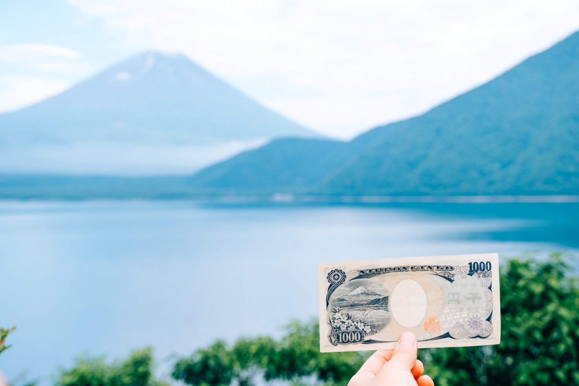 富士山に向かって千円札をかざす